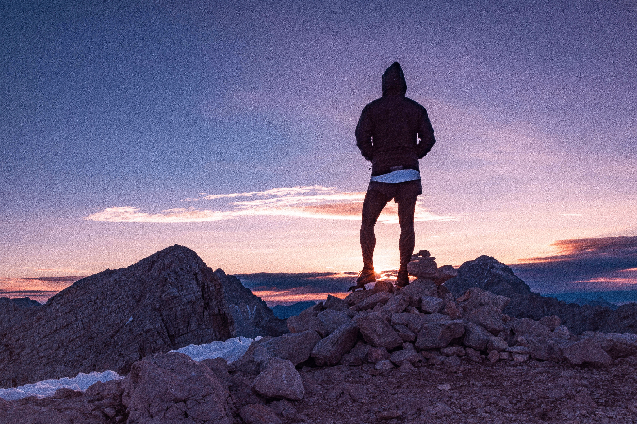 Person standing on a rocky outcrop at sunset with a hooded jacket